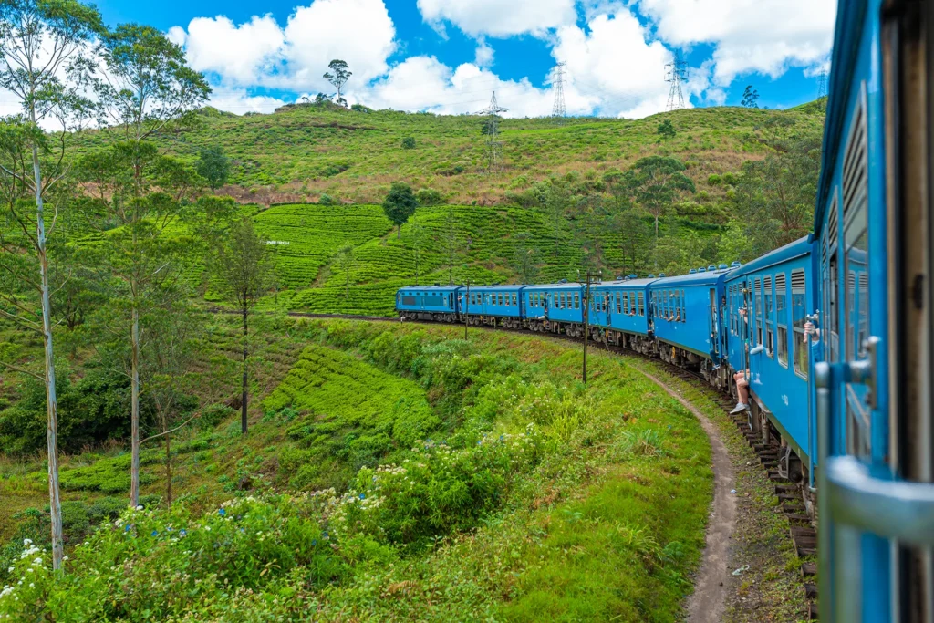 A blue train passing through a misty mountain landscape in Sri Lanka, with lush greenery on both sides.